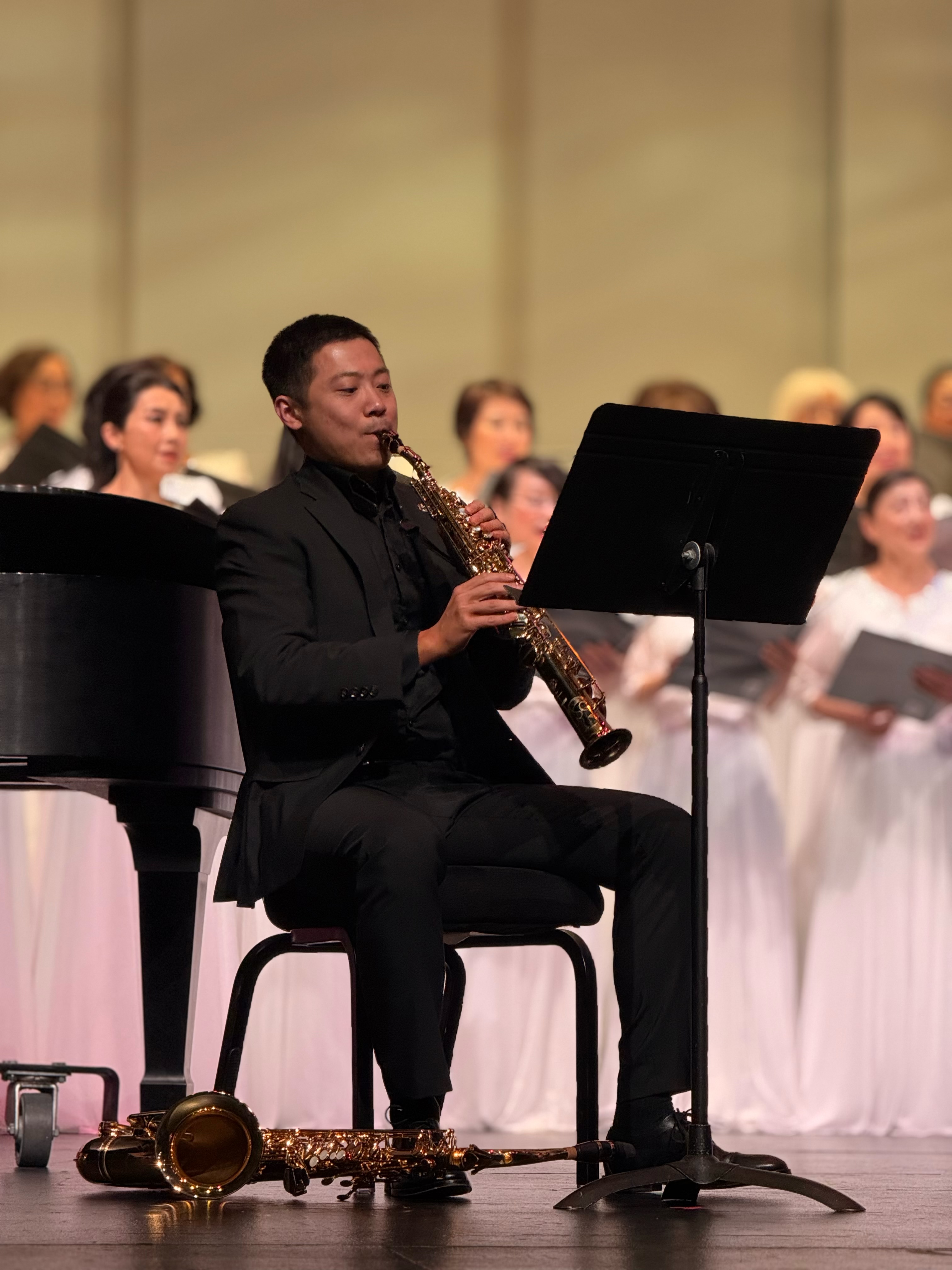 Chen Wang performing saxophone on stage with a choir